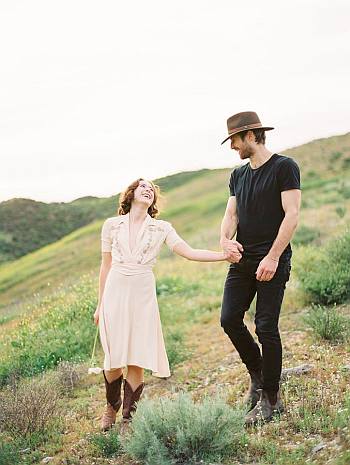 Justin Deeley in a black t-shirt, black pants, and brown hat with his girlfriend in a white dress.